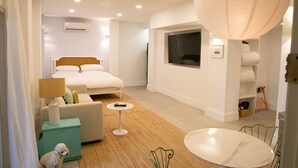 Ein modernes Hotelzimmer mit Bett, Sofa, kleinem Tisch, Fernseher und großem Fenster.