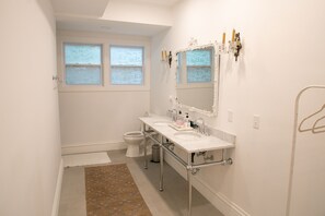 A bathroom with two sinks, a toilet, and a window with frosted glass.