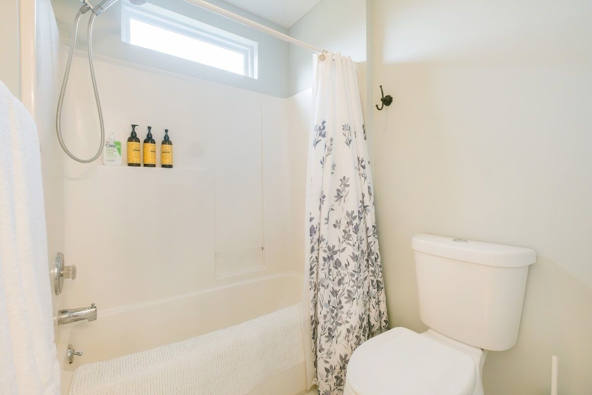 A bathroom with a bathtub, toilet, and shower. There are three bottles on the wall.