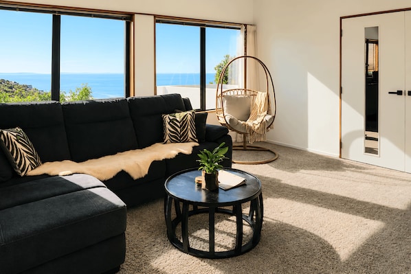 A modern living room with a sofa, a round coffee table, a hanging chair, and a view of the sea.