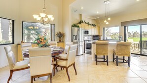 A spacious kitchen with modern appliances, a dining area with a round table and chairs, and large windows offering a view of palm trees. - Community Pools & Golf Views: Palm Desert Condo! (Palm Desert)