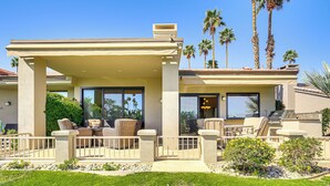 A covered outdoor patio with wicker furniture, a stone pathway, and a view of palm trees. - Community Pools & Golf Views: Palm Desert Condo! (Palm Desert)