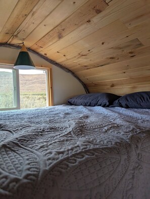 Un dormitorio con techo de madera, un ventanal grande y una cama con colcha estampada.