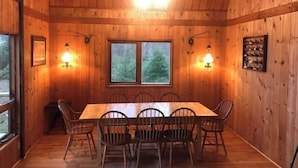 Une cabane en bois avec une table et des chaises, deux fenêtres et des lampes fixées au mur.