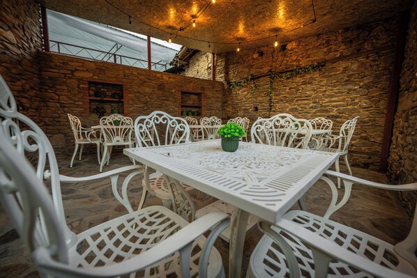 A stone-walled outdoor dining area with white metal chairs and a table, featuring string lights and a potted plant. - FLORA BİRGİ TAŞ KONAK (Odemis)
