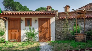 Un bâtiment rustique en pierre, doté de deux portes en bois et d’une petite fenêtre, entouré de verdure et de cactus.