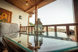 A glass-top table with a lantern, wooden railing, and a view of the outdoors. - FLORA BİRGİ TAŞ KONAK (Odemis)