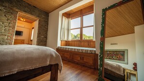 Une chambre à coucher avec un lit en bois, une fenêtre avec des rideaux, un mur en pierre et un miroir doté d’un cadre décoratif.