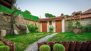 Un bâtiment en pierre avec un toit en tuiles, un chemin menant à des portes en bois et, au premier plan, des cactus en pot.