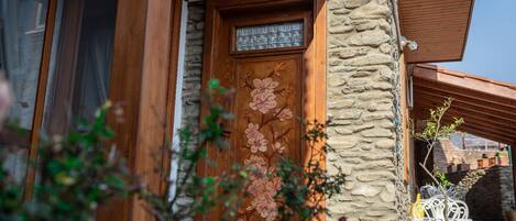 Una puerta de madera con detalles florales, una pared de piedra y una planta en maceta.