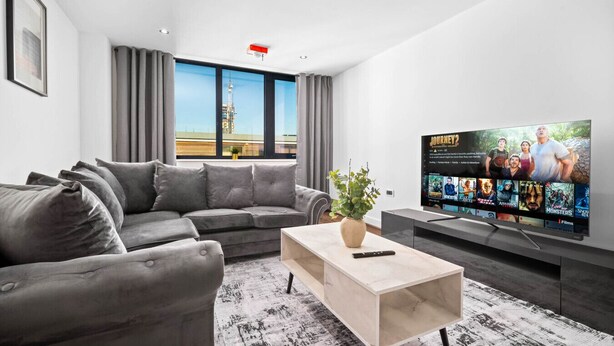 A modern living room with a grey sofa, a coffee table, and a flat-screen TV displaying a movie selection. - Luxury 2 Bed Apartment (Birmingham)