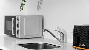 A kitchen with a modern stainless steel sink, a microwave, and a black portable heater. - Luxury 2 Bed Apartment (Birmingham)