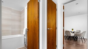 A modern bathroom with a bathtub, wooden doors, and a dining area with a table and chairs. - Luxury 2 Bed Apartment (Birmingham)
