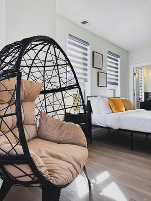 Una habitación con una silla colgante, una cama con almohadas y una ventana con persianas.
