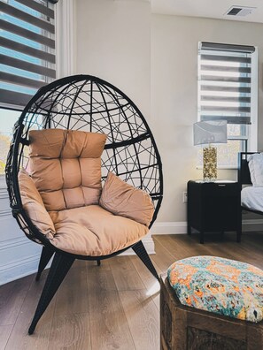 A room with a round, black, woven chair with beige cushions, a small bedside table with a lamp, and a bed with white bedding. - Stylish 3BR Apt w/Laundry Near UPenn&Drexel (Philadelphia)
