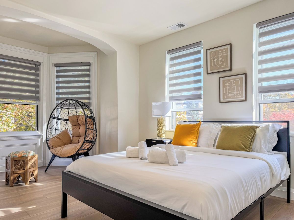 A modern bedroom with a large bed, a hanging chair, and a small wooden stool.