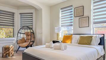 A modern bedroom with a large bed, a hanging chair, and a small wooden stool.