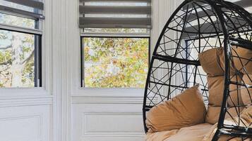 A room with a wooden bench, a wicker chair with cushions, and a window with blinds.