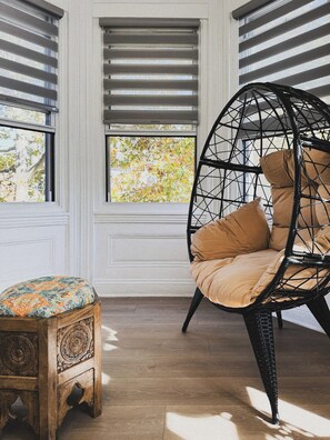 A room with a wooden bench, a wicker chair with cushions, and a window with blinds.