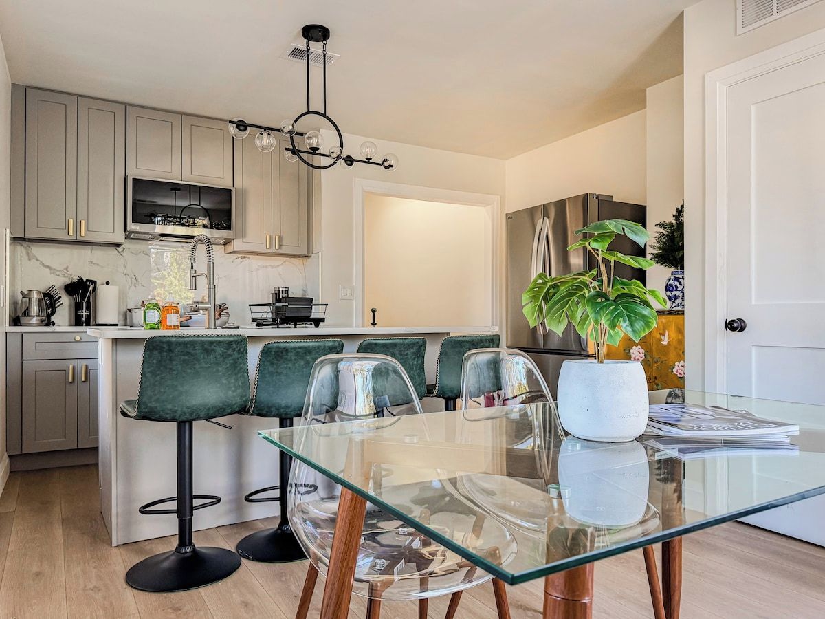 Cozinha moderna com ilha central, banquetas e mesa de jantar com cadeiras.