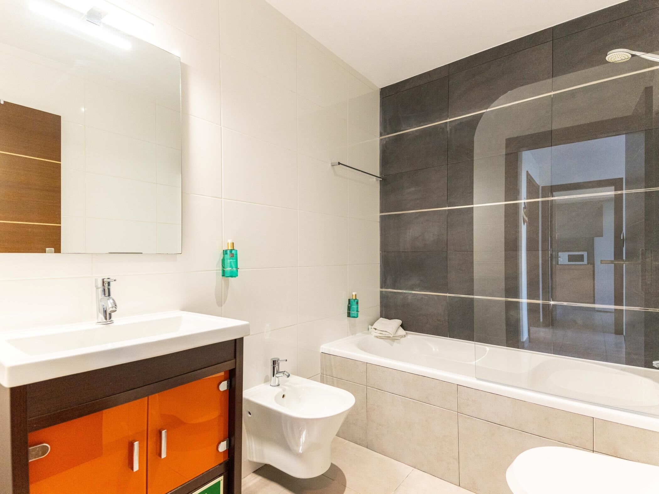 A modern bathroom with a large mirror, two sinks, a bidet, and a bathtub.