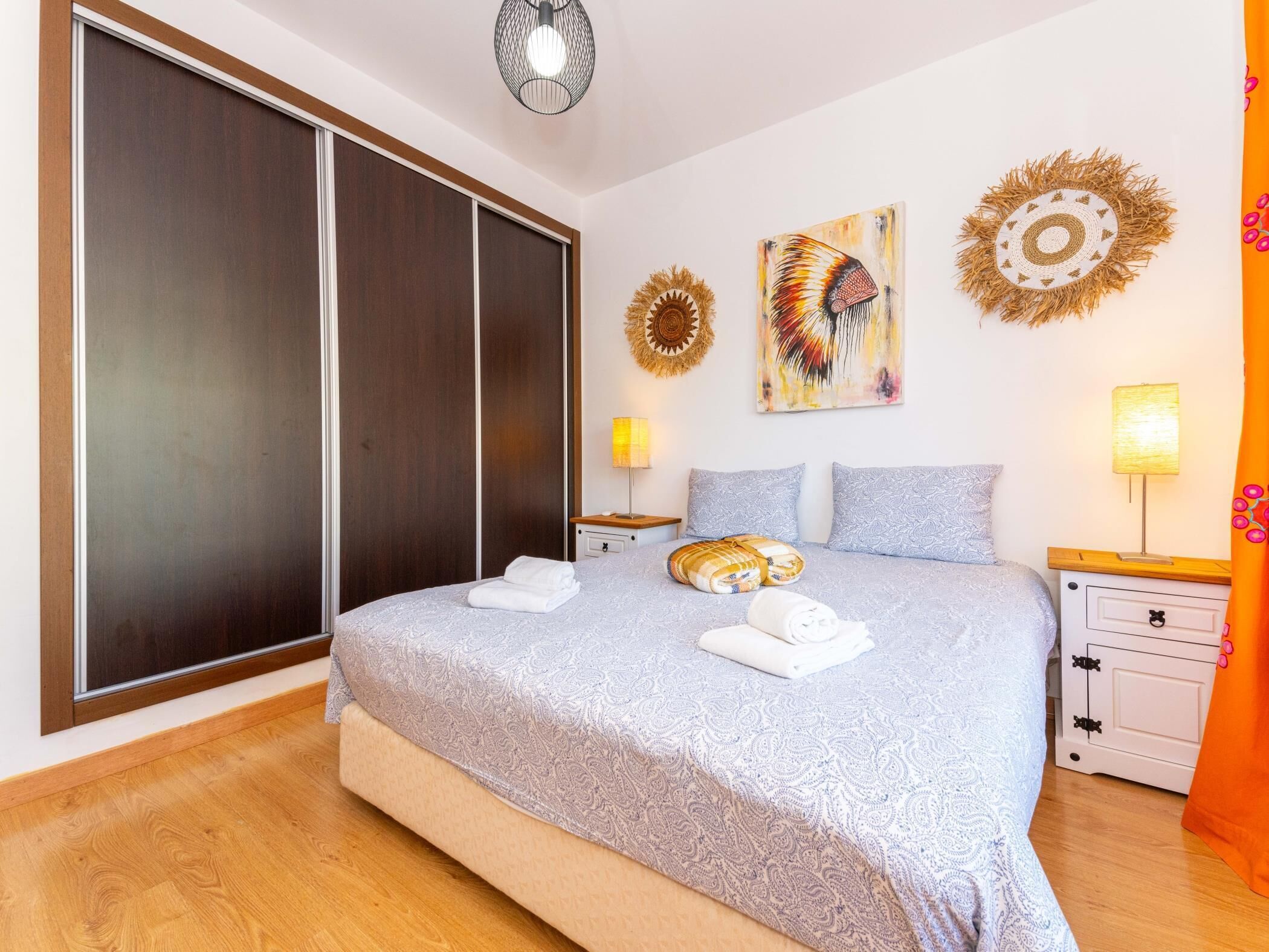 Ein Schlafzimmer mit einem großen Bett, einem Kleiderschrank, zwei Nachttischen mit Lampen und dekorativer Wandgestaltung.