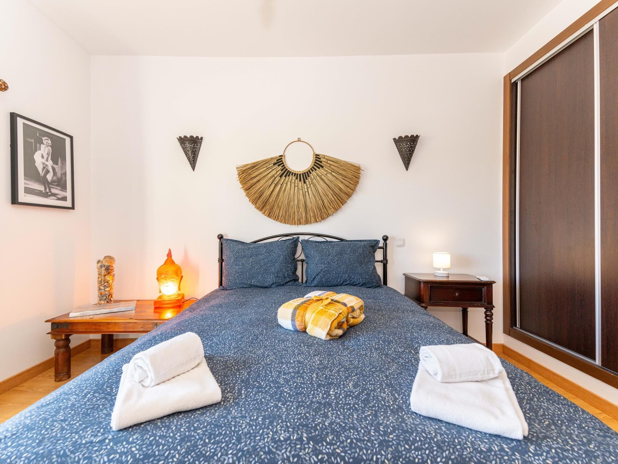 Ein ordentlich bezogenes Bett mit einem blauen, gemusterten Überwurf, zwei Kissen und zwei auf beiden Seiten gefaltete Handtücher.
