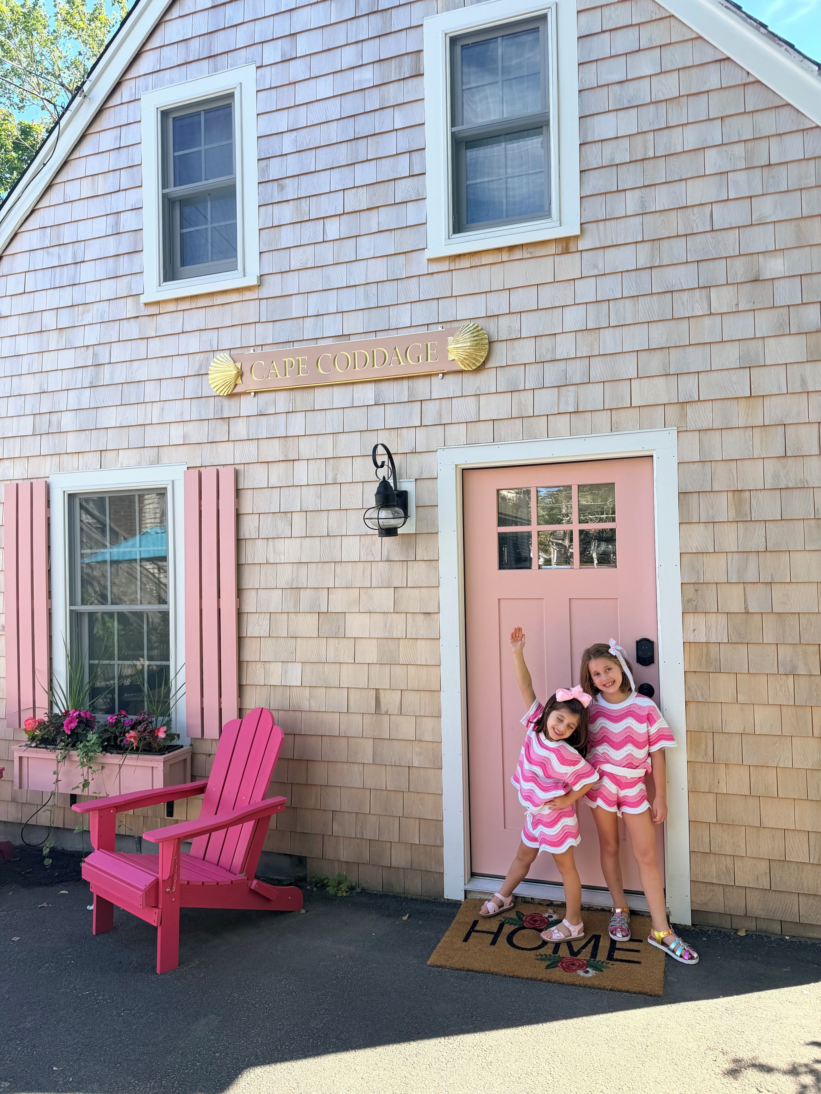 Une maison avec une pancarte indiquant « CAPE CODDAGE », une porte rose et une chaise rouge à l’extérieur.