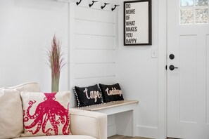 A white wall with a framed motivational quote, a white door, and a bench with decorative pillows. - Town Center-Full Reno 2026-Steps To Shops & Eateries-Walk To Lighthouse Beach (Chatham)