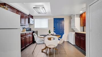 A compact kitchen with wooden cabinets, a white refrigerator, a blue door, and a dining area with white chairs and a round table.