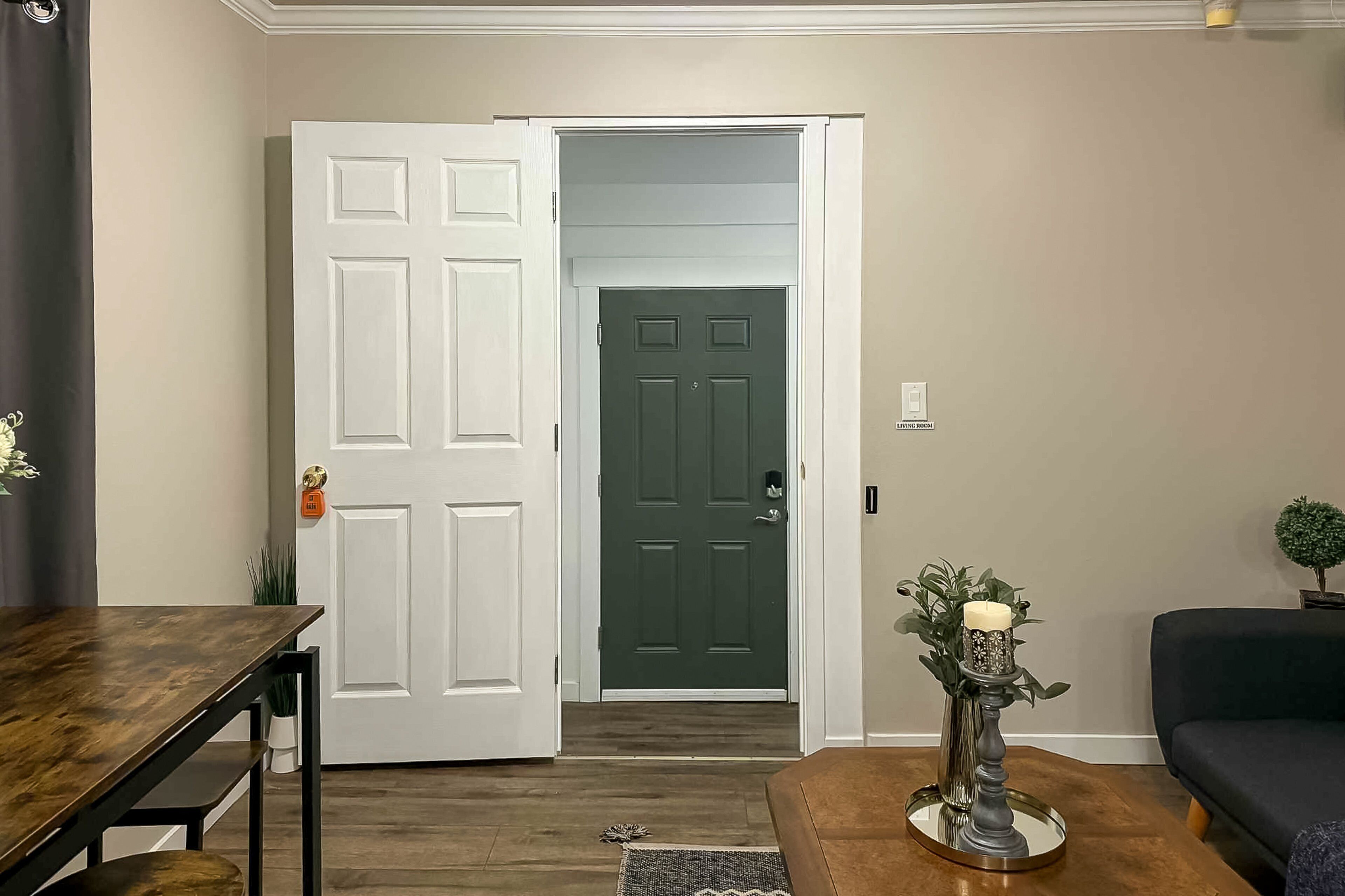 Quarto com uma mesa de madeira, um sofá escuro, uma porta e uma pequena planta.
