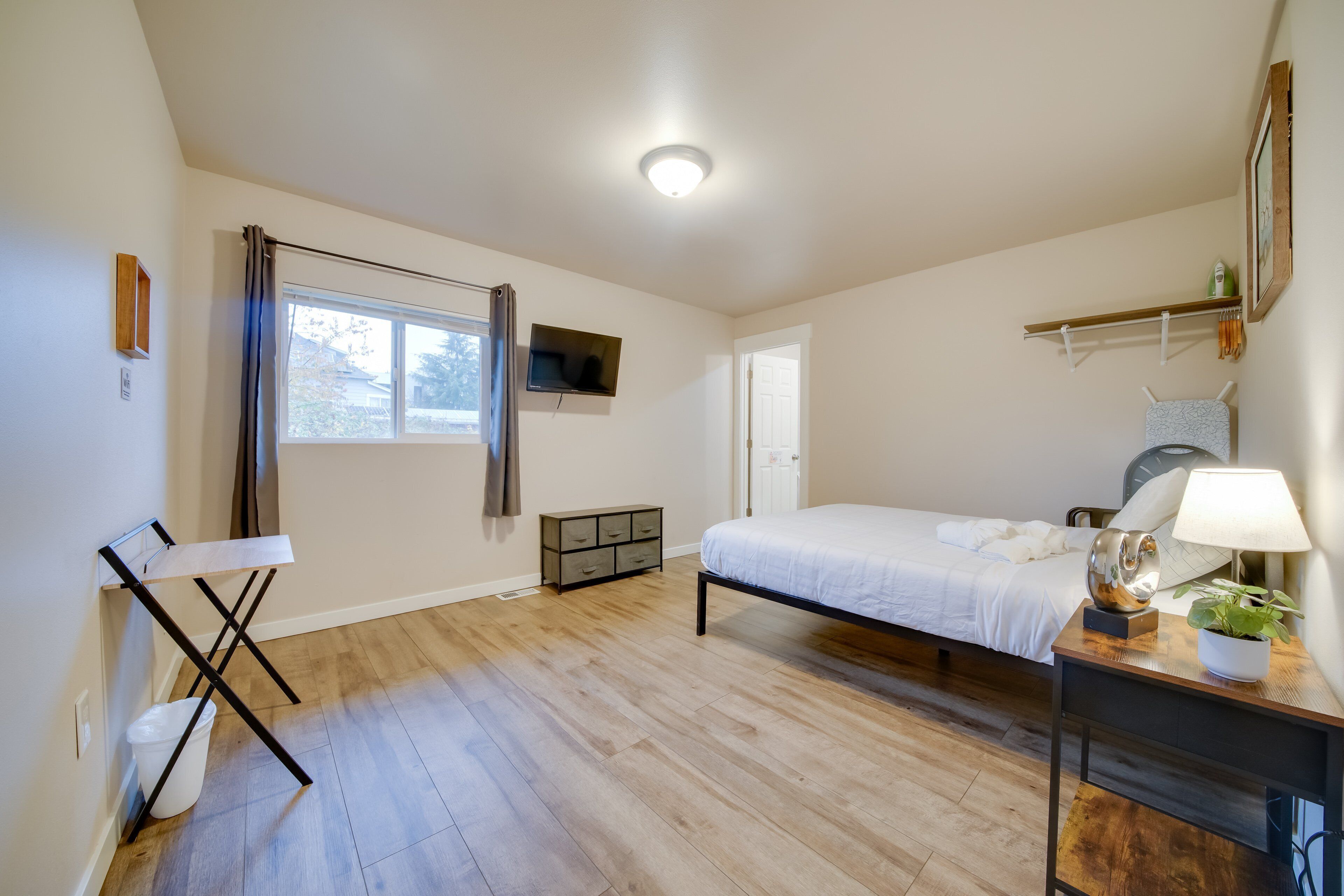 Une chambre à coucher comprenant un lit, une table de chevet, une lampe, une plante en pot et une petite commode.