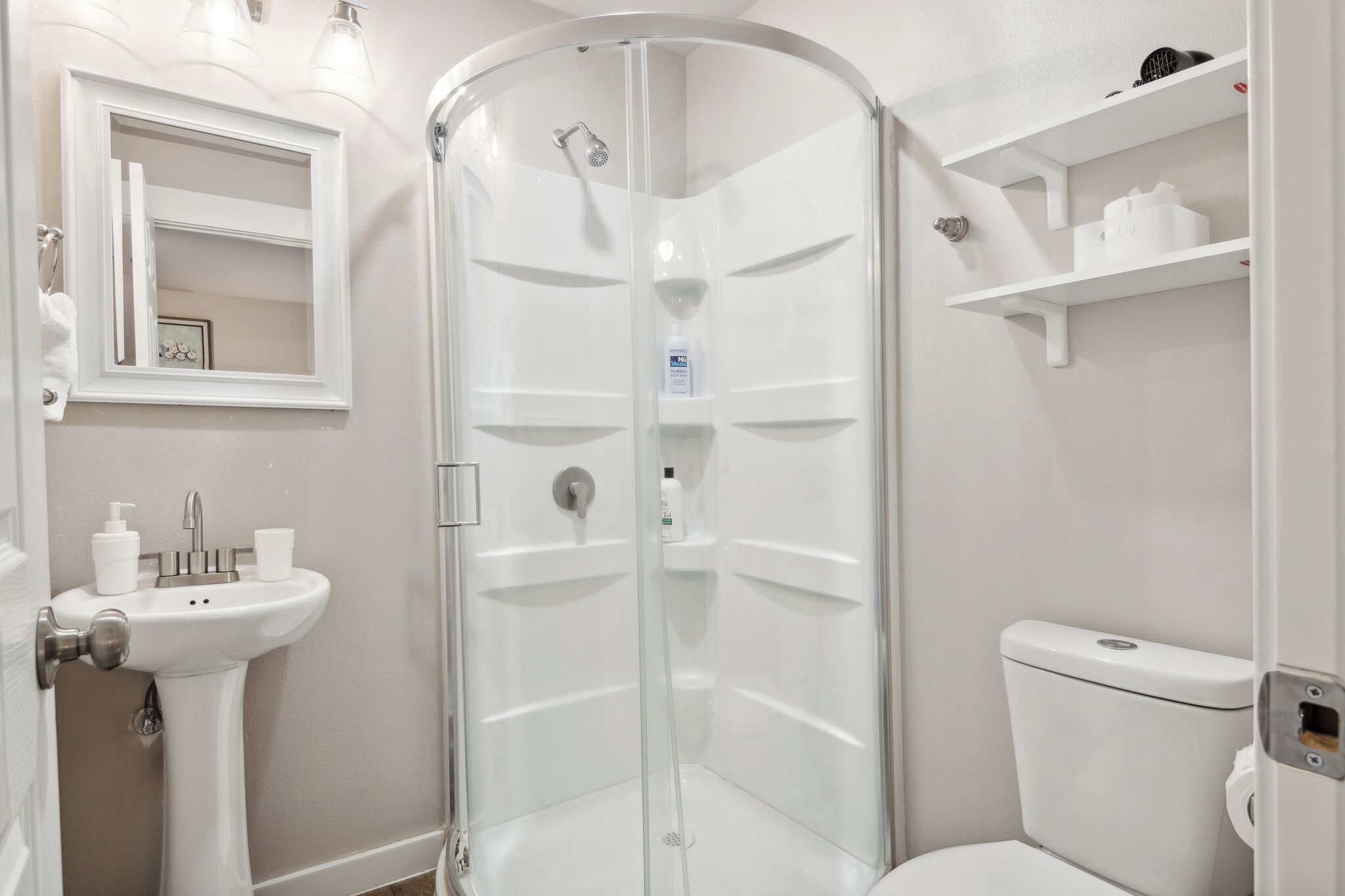 A corner bathroom with a glass shower enclosure, a sink with a mirror, and a toilet.