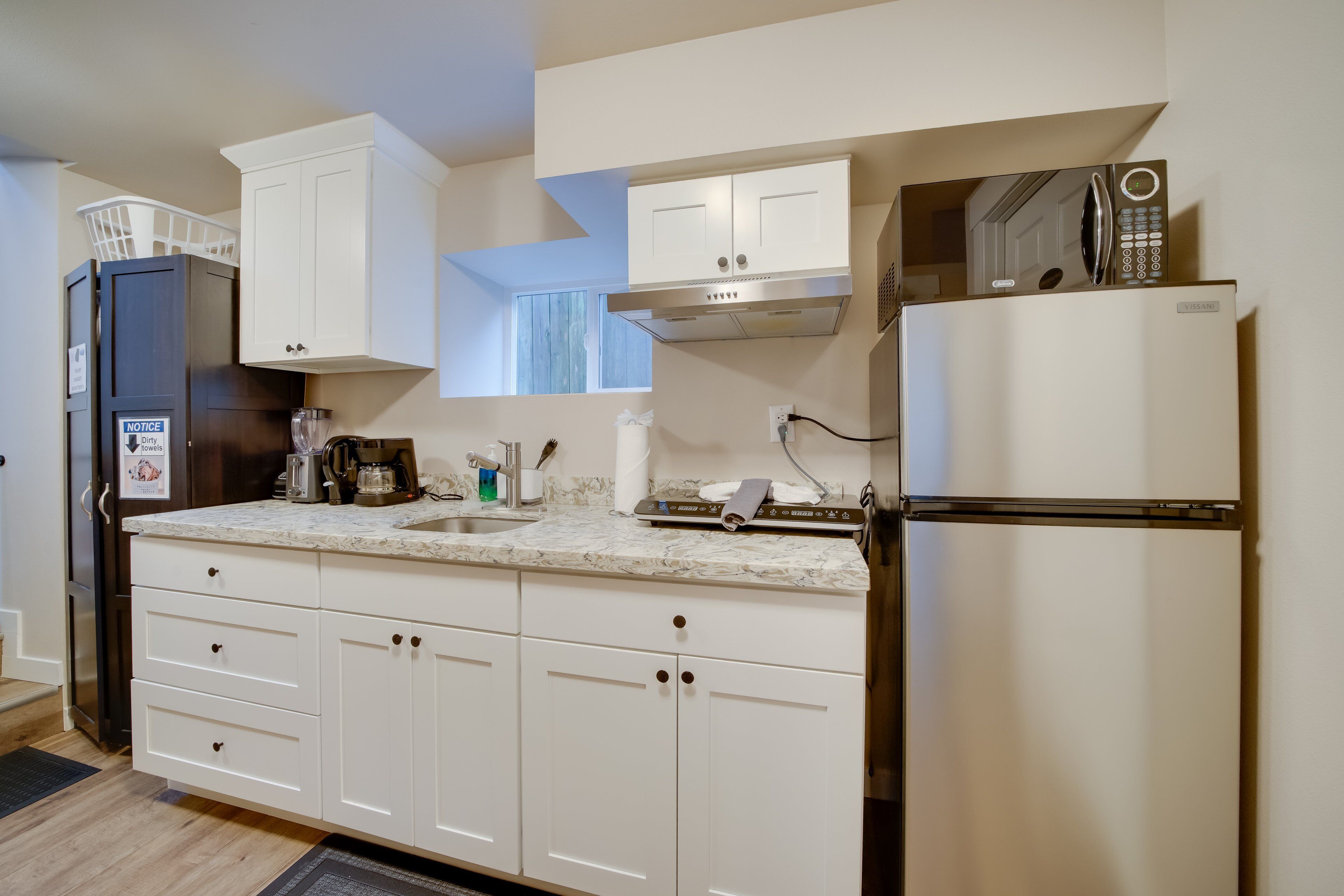A kitchen with white cabinets, a stainless steel refrigerator, a microwave, and a sink.