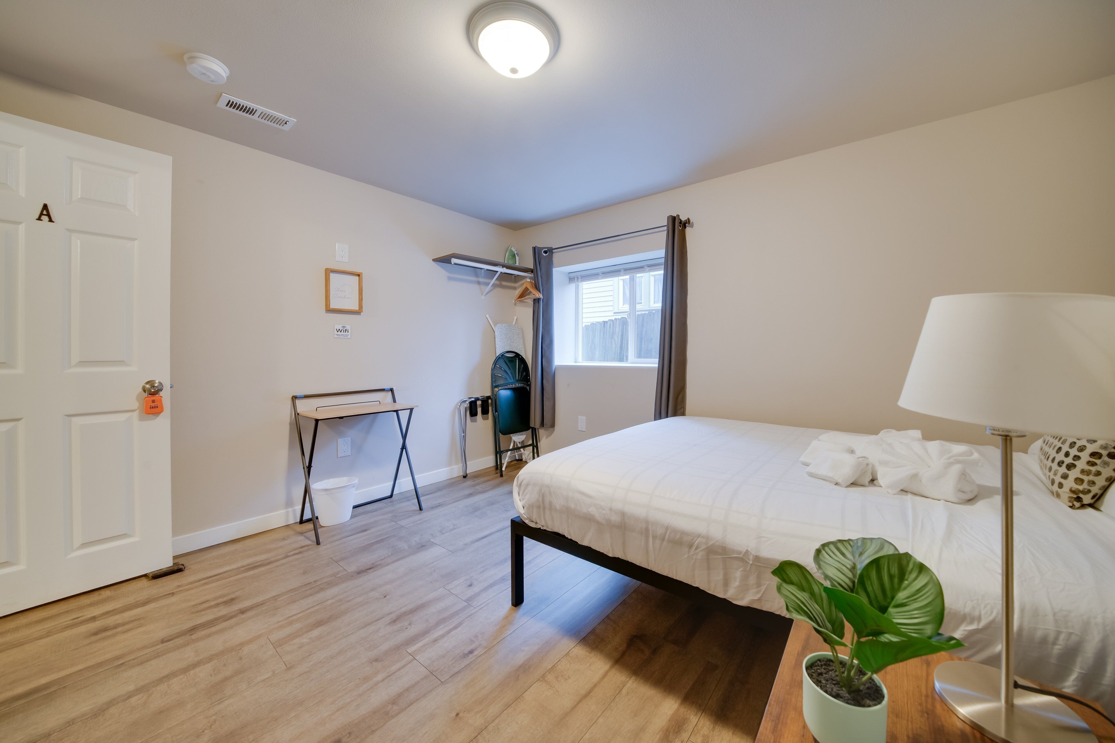A bedroom with a bed, a desk, a chair, a potted plant, a lamp, and a window with curtains.