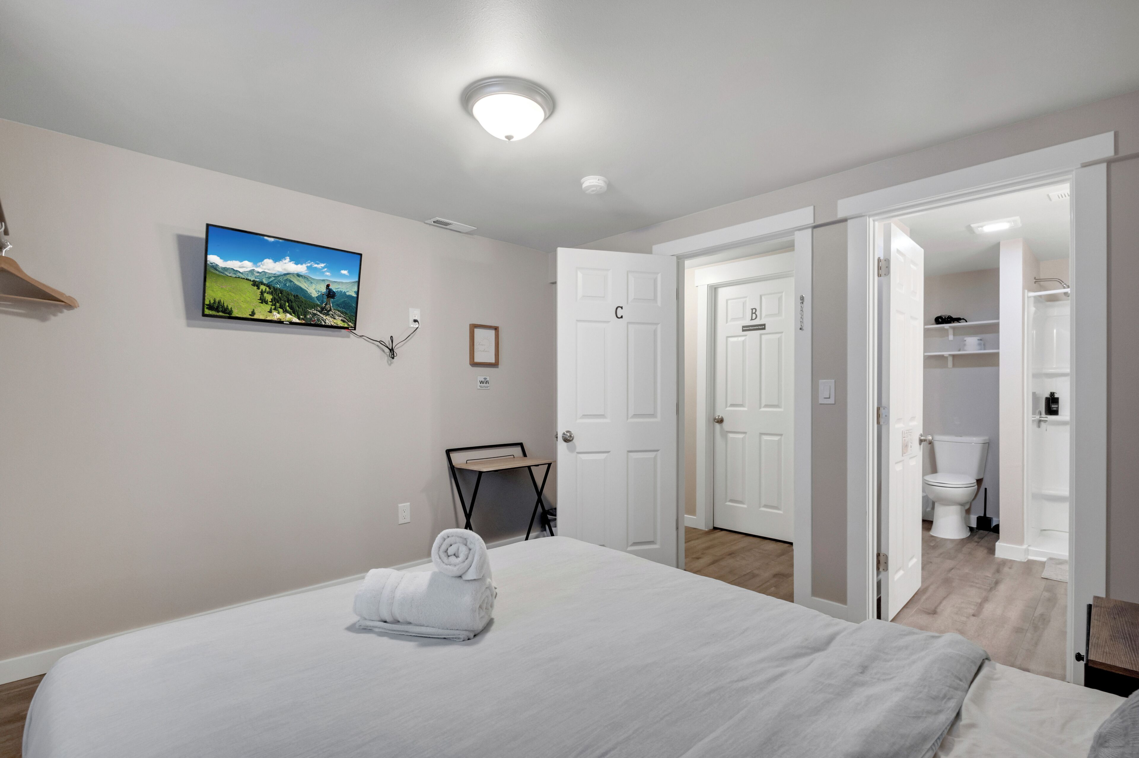 A hotel room with a bed, a TV mounted on the wall, a door leading to a bathroom, and a closet.