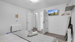 Een hotelkamer met een bed, een aan de muur bevestigde televisie en een deur naar een andere kamer.