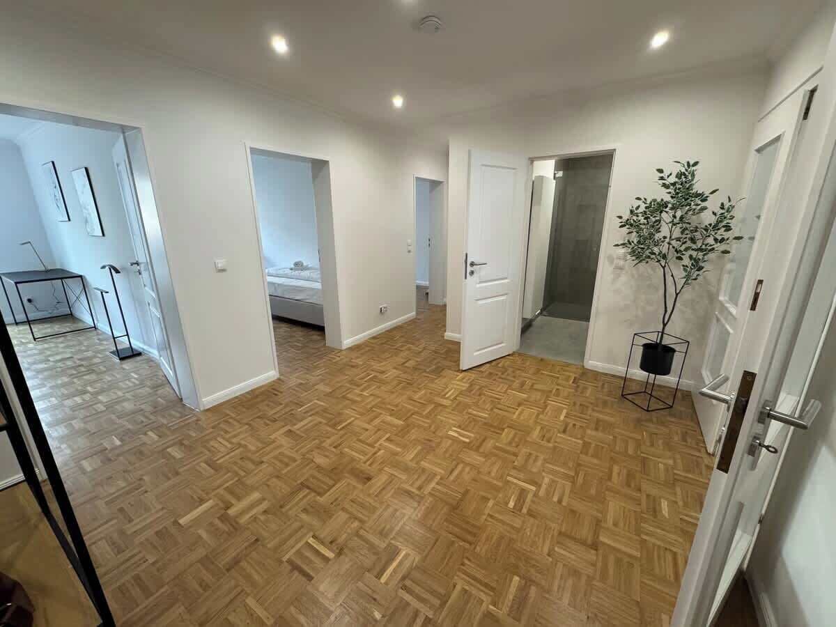 Een ruime kamer met een houten parketvloer, witte muren en een deur naar een andere kamer.