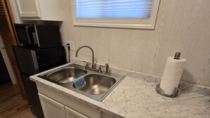 Una cocina con un lavamanos doble, armarios blancos, encimera de mármol y una ventana con persianas.
