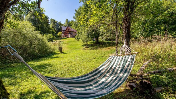 A hammock in a lush green garden with a house in the background.