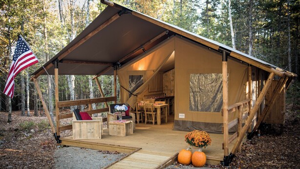 A rustic cabin with a covered porch, wooden furniture, and a small garden with pumpkins. - Accessible, Glamping Tent in Bar Harbor,Just 4 miles from Acadia National Park (Bar Harbor)