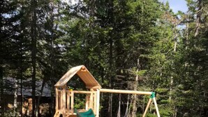 A wooden play structure with a slide and swings in a wooded area. - Accessible, Glamping Tent in Bar Harbor,Just 4 miles from Acadia National Park (Bar Harbor)