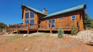 Une cabane en bois dotée d’une grande terrasse, de nombreuses fenêtres et d’un toit végétalisé.