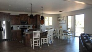 A spacious kitchen with wooden cabinets, a stainless steel refrigerator, and a dining area with white chairs and a table. - Zion views- R Family Square + Resort Access (Orderville)