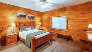 Ein Schlafzimmer einer Holzhütte mit einem Bett, zwei Nachttischen, einem Deckenventilator und einem Fenster mit Jalousien.
