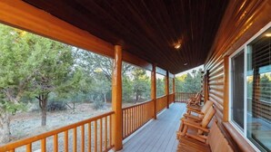 Eine überdachte Veranda mit Holzgeländern und Bänken, die auf eine natürliche Landschaft mit Bäumen und blauem Himmel blickt.