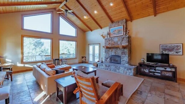 Un salón amplio con chimenea de piedra, ventanas grandes y un techo alto con vigas de madera.