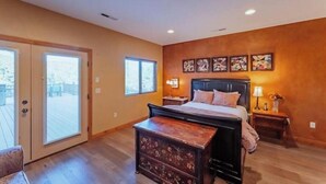 Un dormitorio con cama, cómoda y mesita de noche. Hay dos ventanas y un ventanal corredero que da a un balcón.