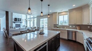 Une cuisine moderne dotée d’un grand îlot central, d’appareils électroménagers en acier inoxydable et de luminaires suspendus.
