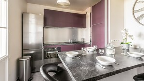 A modern kitchen with a central island, stainless steel appliances, and purple cabinets. - Apartment Les Alizés  (Bailly-Romainvilliers)